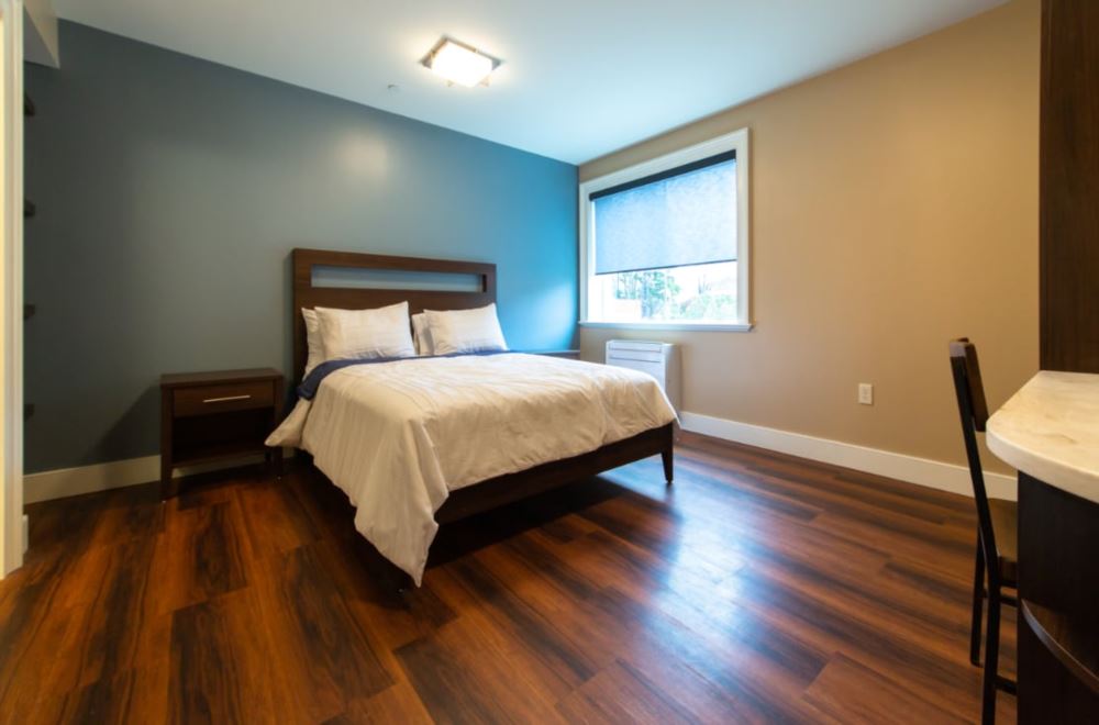 a twin bed in a patient room with wooden flooring and slate blue walls